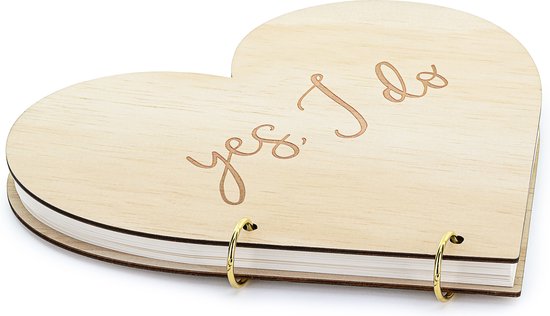 Houten gastenboek in hartvorm met de tekst 'yes, I do' gegraveerd. Gouden ringband. Op een roze achtergrond.