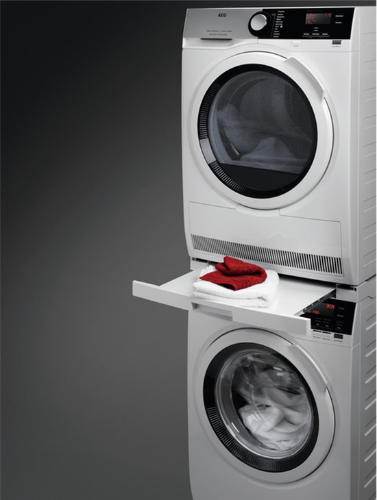 Witte AEG wasmachine en droger gestapeld met een witte lade ertussen, met rode en witte handdoeken erop.