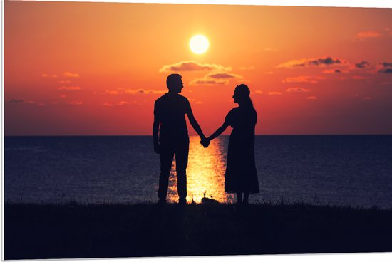 PVC Schuimplaat- Silhouet van Koppel Hand in Hand bij de Zee tijdens Zonsondergang - 90x60 cm Foto op PVC Schuimplaat