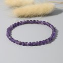 Armband van kleine, paarse amethistkralen op een grijze achtergrond met zachte pluimen.