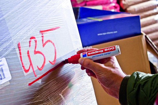 Hand schrijft met rode Edding 800 marker cijfer '435' op een ingepakt pakket.