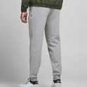 Man in een lichtgrijze joggingbroek, groene bomberjack en bruine hoodie, met witte sneakers.