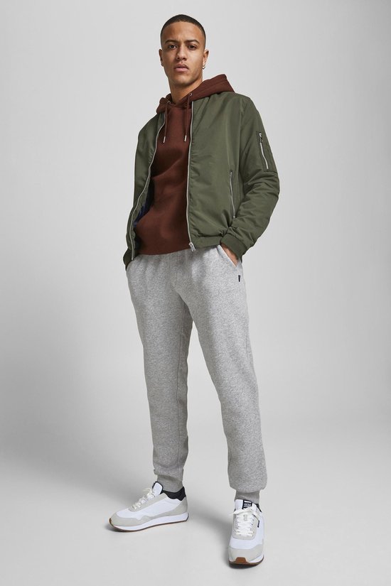 Man met lichtgrijze joggingbroek, bruine hoodie en groene jas.