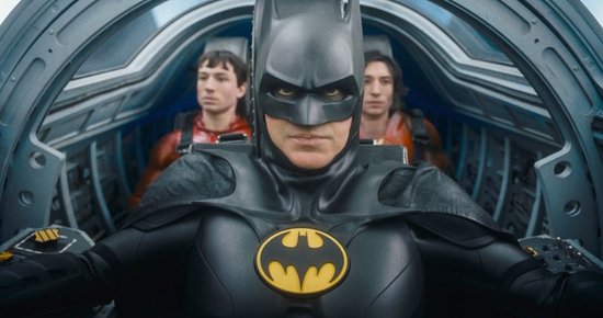 Batman in een zwart pak, met twee mannen in rode supersuits op de achtergrond.