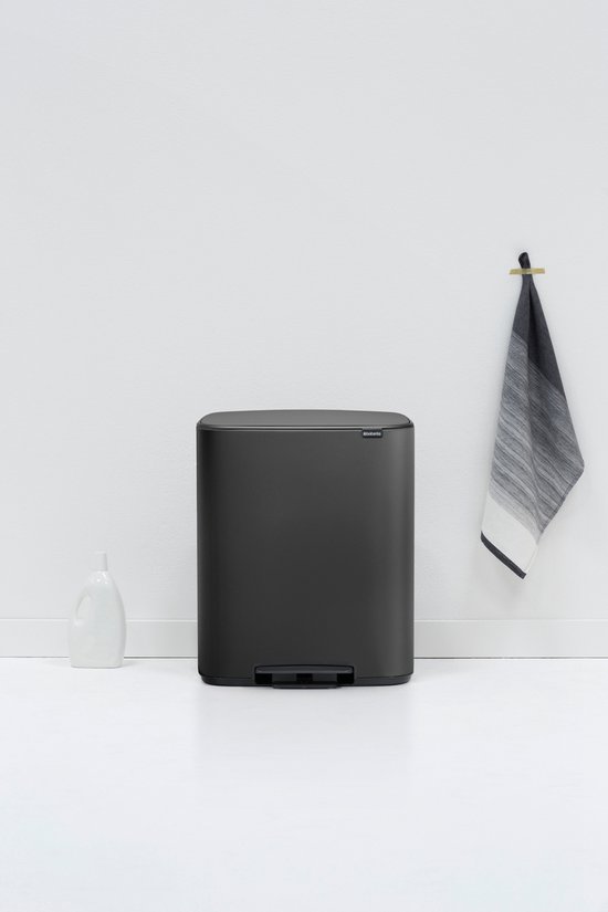 Donkergrijze Brabantia prullenbak met gebogen bovenrand en voetpedaal, in een minimalistische keuken.