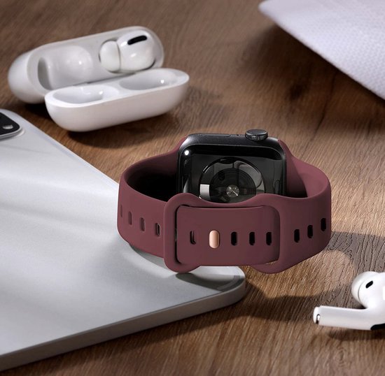 Bordeauxrood siliconen horlogebandje, opengewerkt, met gesp, naast Apple Watch en oordopjes.