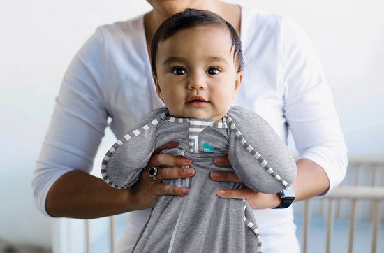 Baby in grijze Love to Dream™ Swaddle Up™ met witte strepen, omhoog gehouden door een persoon.