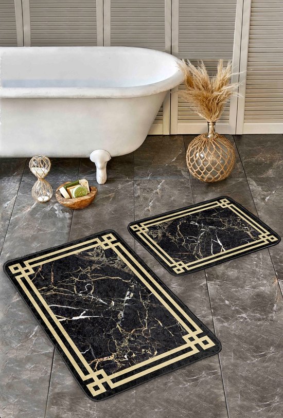 Twee zwarte badmatten met marmerprint en gouden geometrische rand, op een donkergrijze tegelvloer bij een wit bad.
