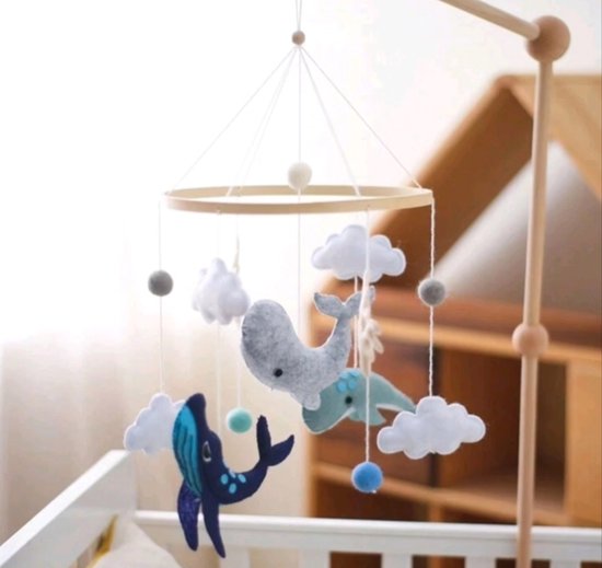 Houten babybed hanger met vilten decoraties: grijze walvis, blauwe walvis, mintgroene walvis, wolken, koraal en ballen, hangend boven een ledikant.