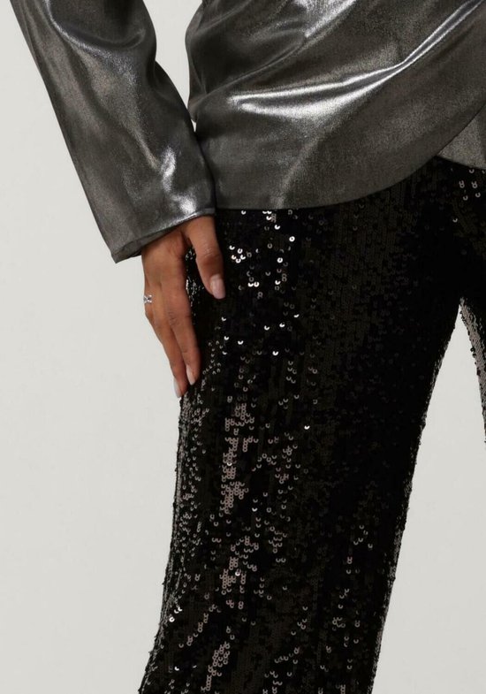 Model draagt een broek met zwarte pailletten en een zilverkleurig glanzend jasje.