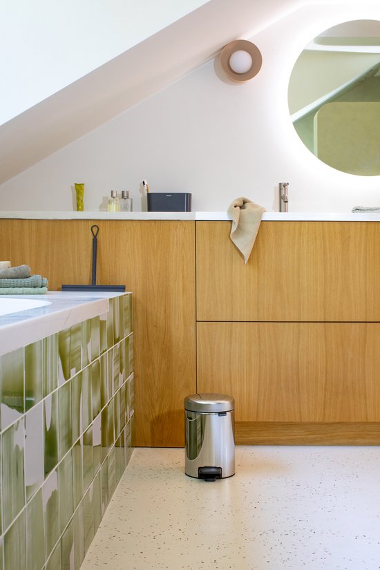 Briljant stalen Brabantia NewIcon prullenbak met zwart voetpedaal, in een moderne badkamer met houten kast.