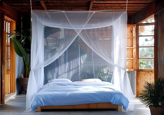 Wit klamboe met een dubbele opening, hangend boven een bed met blauw beddengoed in een zonnige kamer.