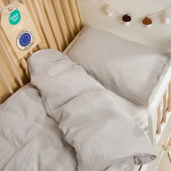 Grijs moslin katoenen beddengoed in een babybedje, inclusief OEKO-TEX label.