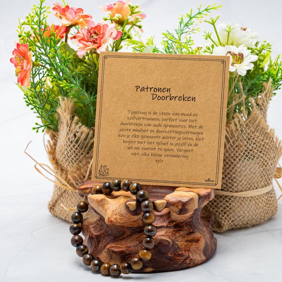Tijgeroog armband op een houten display met een cadeaukaartje, omringd door bloemen.