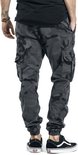 Model in donkere camouflage cargo broek met zakken en zwarte Vans sneakers.