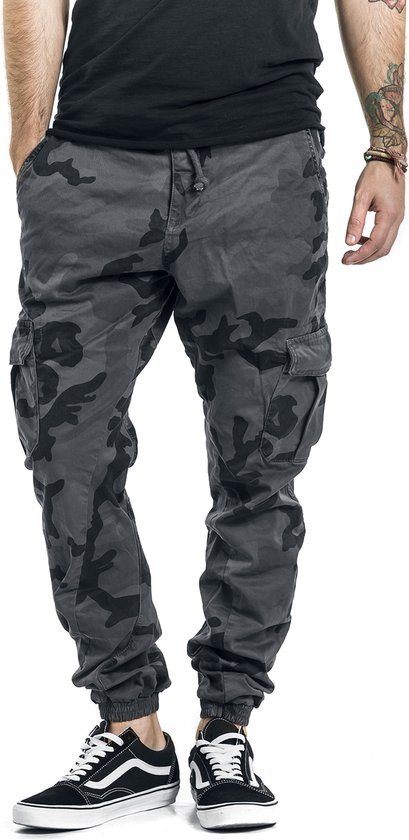 Mannelijke cargobroek met camouflageprint in grijs en zwart, met trekkoord en zakken. Gedragen met Vans sneakers.