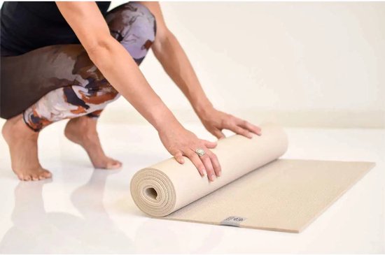 Een vrouw met een patroon legging rolt een beige yogamat uit.