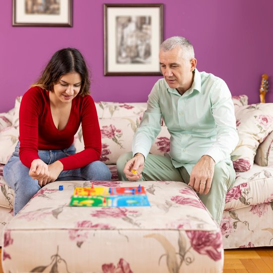 Een jonge vrouw en een oudere man spelen samen een bordspel met kleurrijke vakjes.