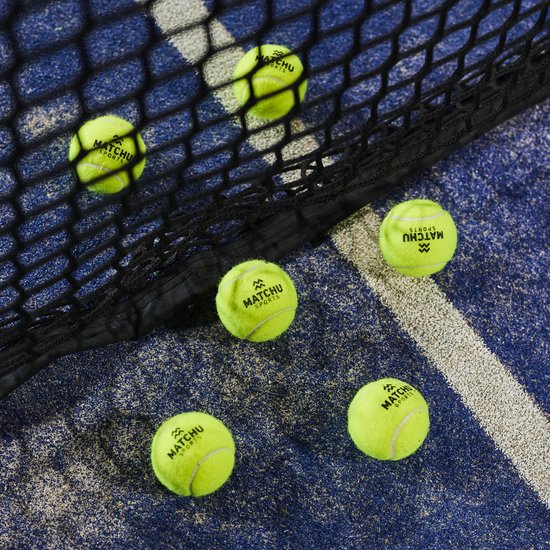 Vier gele padelballen van Matchu Sports liggen op een blauwe padelbaan, met een zwart net op de voorgrond.
