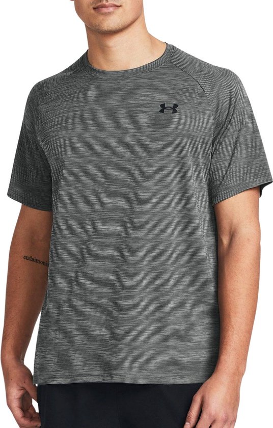 Man draagt grijs sportshirt met fijne horizontale strepen en zwart Under Armour logo op de borst.