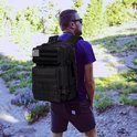 Man met zwarte tactische rugzak met Amerikaanse vlag patch, wandelend in de natuur.