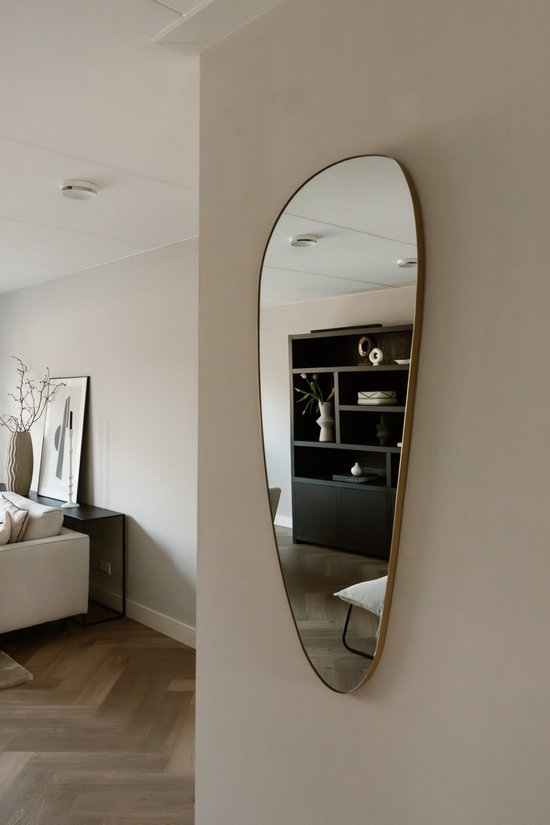 Organische, asymmetrische wandspiegel met gouden rand in een woonkamer