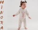 Een schattig meisje met krullend haar en strikjes in het haar draagt een gebreid rompertje in de kleur off-white met een roze konijnenprint op de borst en een wit pompon-staartje.