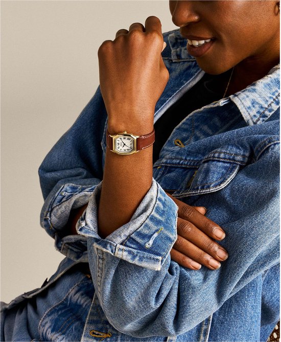 Model met een gouden Fossil horloge met crèmekleurige wijzerplaat en bruin leren bandje om de pols.