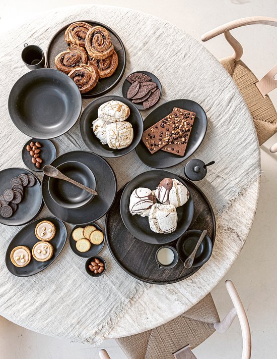 Zwart servies op tafel met gebakjes, chocolade en koekjes.