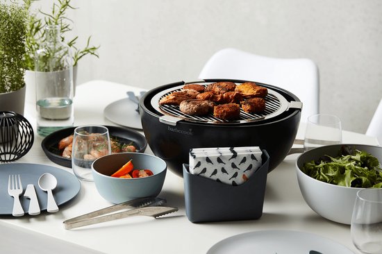 Zwarte tafelgrill met gegrild vlees, kip en worstjes, op een tafel met salade en brood.