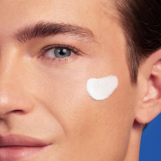Close-up van een mannelijk gezicht met een witte veeg crème op de wang.
