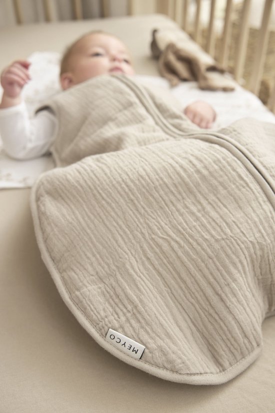 Drie baby slaapzakken hangen aan een rek: groen, grijs en zandkleurig. De zandkleurige slaapzak is gevoerd.