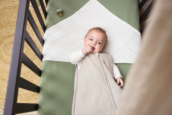 Baby in een lichtgrijze Meyco slaapzak liggend in een wieg, kijkend naar de camera.