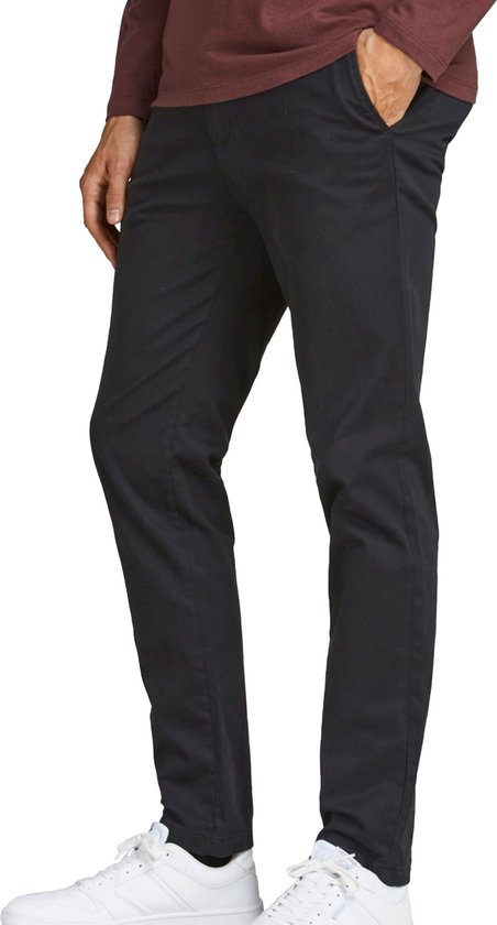 Man, zijkant, draagt bordeauxrode longsleeve, zwarte chino, witte sneakers.