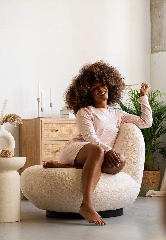 Vrouw met afro-haar in een lichtroze gestreept nachthemd, zittend in een stoel.