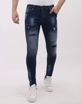 Model in blauwe slim fit jeans met gescheurde details en witte sneakers.