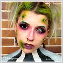 Een vrouw met groen geverfd haar, make-up en kostuum, draagt een zwarte lens in het ene oog en een witte lens in het andere.