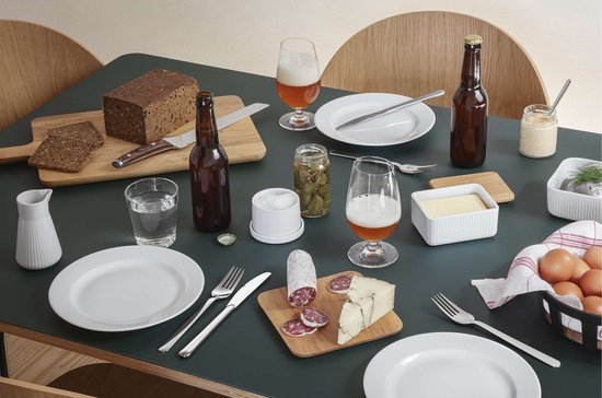 Une table remplie de nourriture, y compris du pain, de la saucisse, du fromage, des œufs, de la bière et un beurrier.