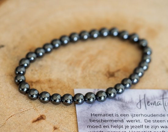 Een zwarte, glanzende hematiet kralenarmband op een houten ondergrond met een kaartje.
