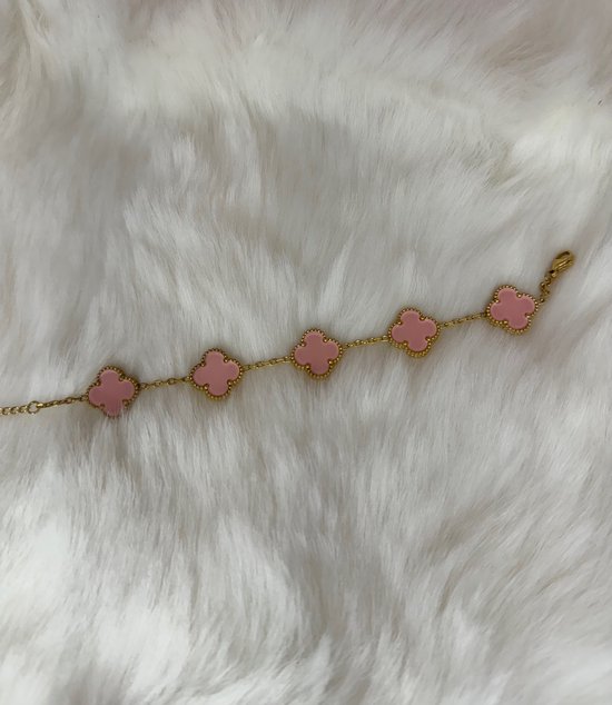 Gouden armband met vijf roze klavervormige bedels op een witte, pluizige achtergrond.