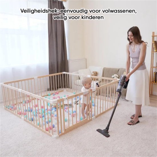Een vrouw stofzuigt naast een houten babybox met een kind erin.