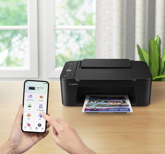 Zwarte Canon Pixma printer op een houten bureau, met een smartphone en een geprinte brochure.