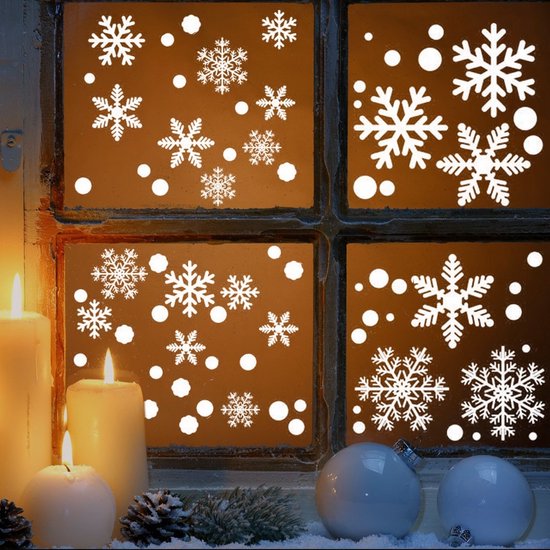Witte kerst raamstickers met sneeuwvlokken en cirkels op een donker raam, naast kaarsen en kerstballen.
