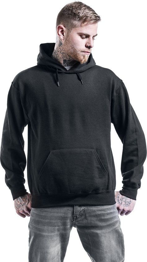 Man met tatoeages draagt een zwarte hoodie met capuchon en grijze jeans.
