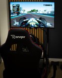 Zicht vanaf een racestoel naar drie monitoren die een racegame tonen. Het 'Ranqer'-logo is zichtbaar op de hoofdsteun.