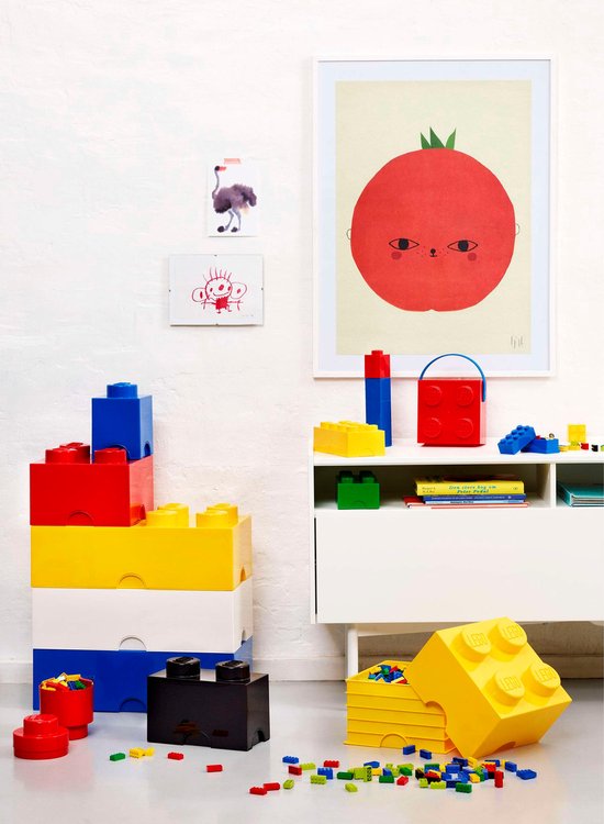 Boîte de rangement LEGO jaune avec couvercle, à côté d'une armoire blanche avec des boîtes rouges et bleues.