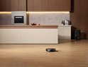 Zwarte robotstofzuiger met dubbele dweilkoppen op een houten vloer in een moderne keuken.