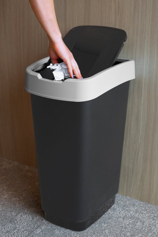 Een hand gooit een stuk papier weg in een zwarte prullenbak met grijze rand.