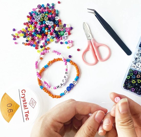 Handen maken een armband met kleurrijke letterkralen. Een schaar en pincet liggen naast de kralen.