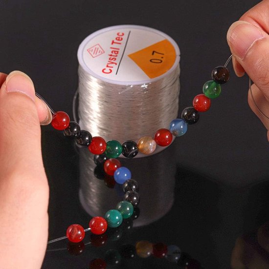 Hand rijgt veelkleurige kralen aan transparant elastisch rijgdraad van 'Crystal Tec'.